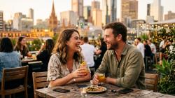 Young Australian couple laughing together over cocktails at a rooftop bar at golden hour